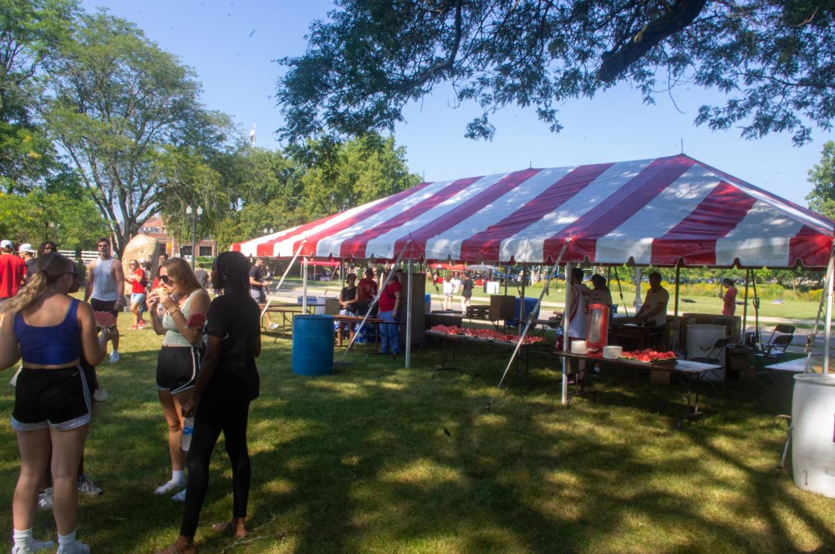  2024 President’s Picnic event goers eat watermelon in front of the watermelon and cookie tent. Other than food, the event included yard games, canoeing, kayaking and different sample tents for Bubbl’r and Celsius drinks. (Sam Dion | Northern Star) 
