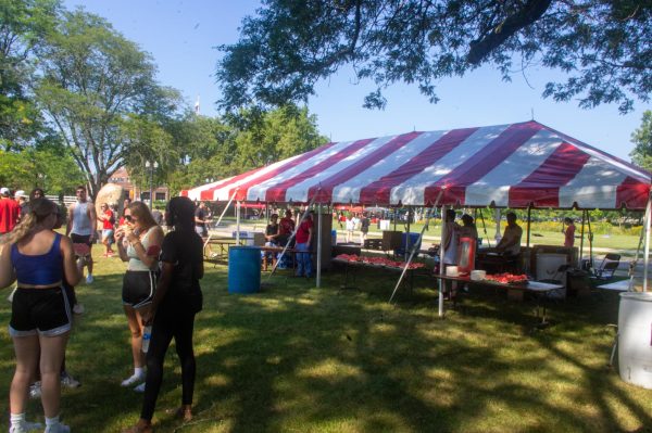  2024 President’s Picnic event goers eat watermelon in front of the watermelon and cookie tent. Other than food, the event included yard games, canoeing, kayaking and different sample tents for Bubbl’r and Celsius drinks. (Sam Dion | Northern Star) 
