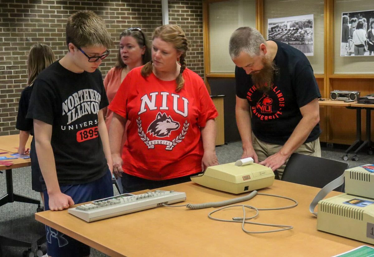 Nathan Bernhard (from left), Heather Bernhard and Rob Bernhard from Crystal Lake, IL work together to figure out what they need to type on a keyboard to get a code. The Founders Memorial Library hosted an 80s themed escape room Saturday during Family Weekend. (Marco Alvarez | Northern Star)