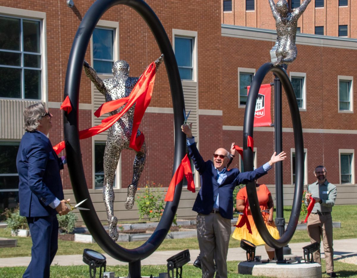 Robert Brinkmann, dean of the College of Liberal Arts and Sciences, and Paul Kassel, dean of the College of Visual and Performing Arts cheer after they cut the ribbon on the middle sculpture at the Stevens Building. The Stevens Sculpture dedication event occurred at 11 a.m. on Thursday. (Katherine Follmer | Northern Star)