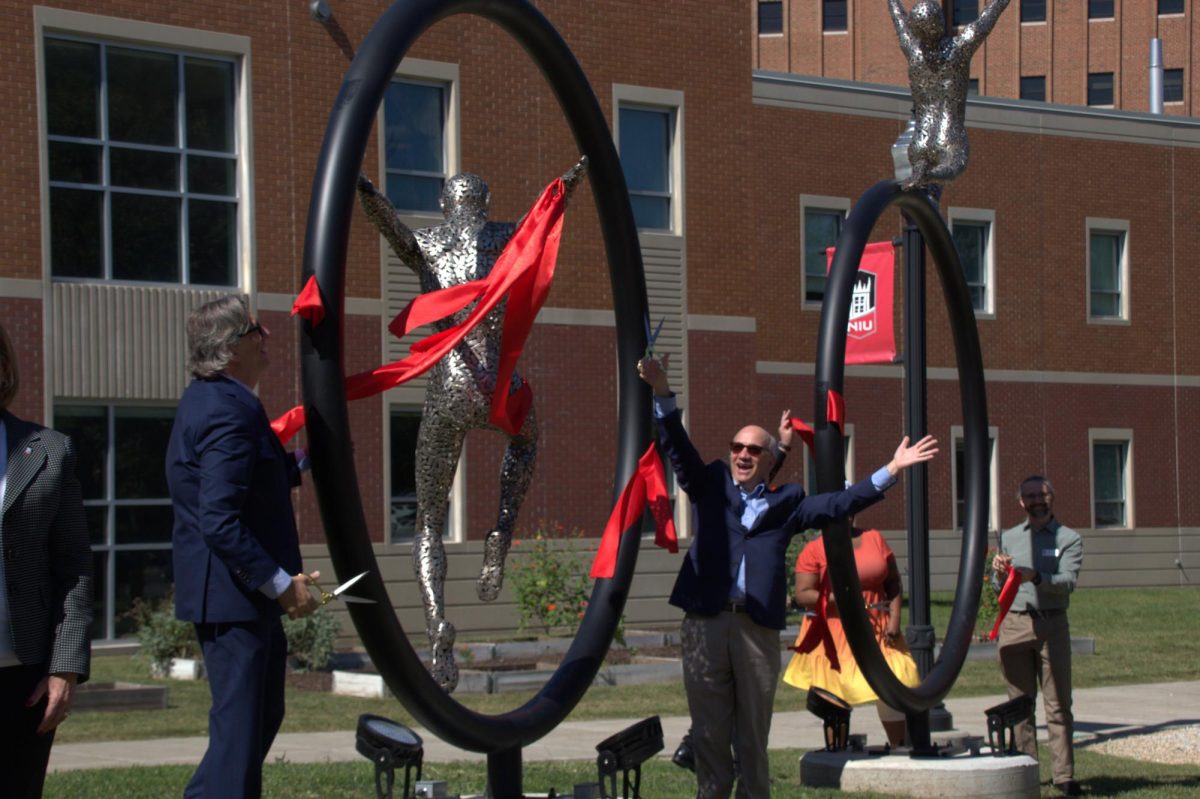 Robert Brinkmann, dean of the College of Liberal Arts and Sciences, and Paul Kassel, dean of the College of Visual and Performing Arts cheer after they cut the ribbon on the middle sculpture at the Stevens Building. The Stevens Sculpture dedication event occurred at 11 a.m. on Thursday. (Katherine Follmer | Northern Star)