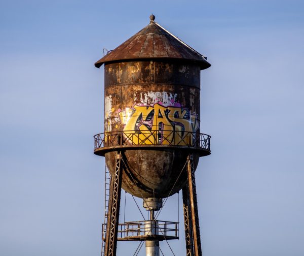 An old brown water tower is marked with gold graffiti lettering on Pleasant Street next to the Forge Resources Group in DeKalb. Without obtaining permission ahead of time, graffiti may be defined as vandalization instead of art. (Tim Dodge | Northern Star)