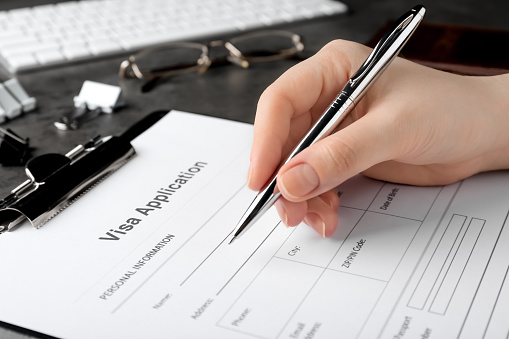 A person is filling out a visa application that is attached to a clipboard. Indian graduate student enrollment has decreased due to visa delays. (Getty Images)