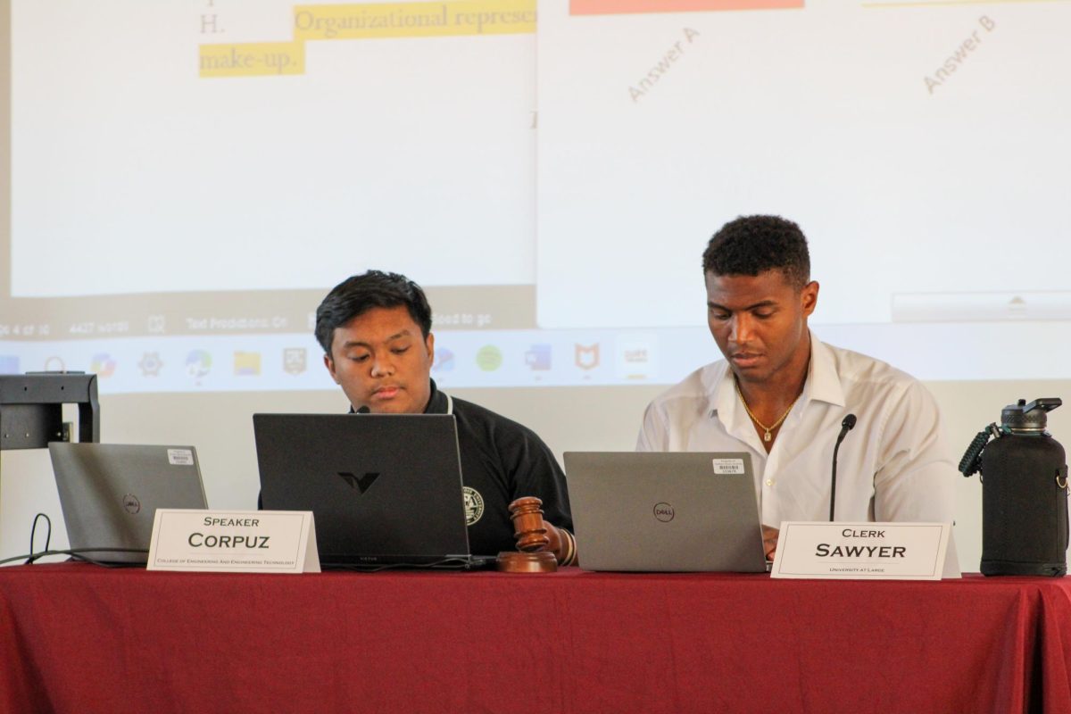 Speaker Manny Corpuz and Clerk Cameron Sawyer sit at a table while Speaker Corpuz bangs the gavel on the table. SGA proposed a bill to allow senators to speak to the press, which will be voted on at the next meeting. (Ethan Rodriguez | Northern Star)