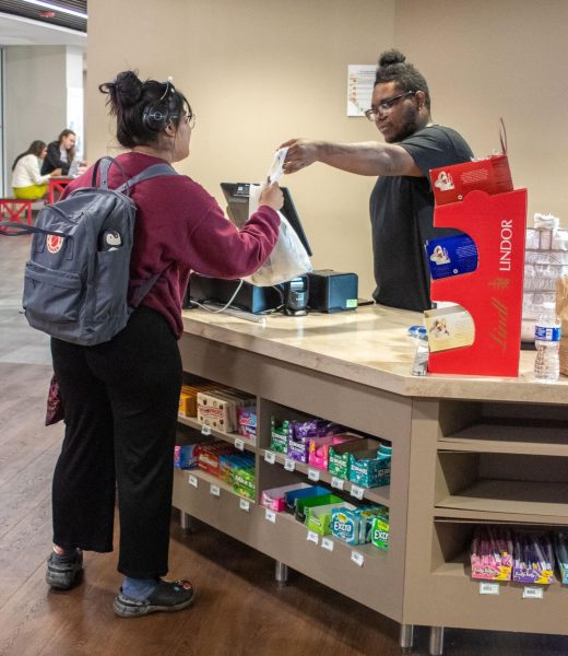 Walter Edwards, a Residential Dining Service cashier, hands a bag to a student in the Depot at the Holmes Student Center. If areas are not in compliance with health code regulations, the violated area gets marked on the report. (Marco Alvarez | Northern Star)