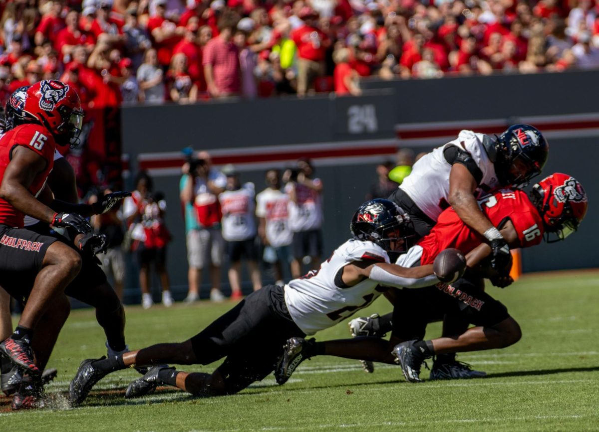 NIU senior linebacker Jaden Dolphin (26) and redshirt junior defensive end Pierce Oppong (99) force a fumble by North Carolina State University freshman quarterback CJ Bailey (16) on NC State’s opening possession in Saturday’s game at Carter-Finley Stadium in Raleigh, North Carolina. The Huskies lost the turnover battle by four after losing two fumbles and tossing two interceptions. (Tim Dodge | Northern Star)