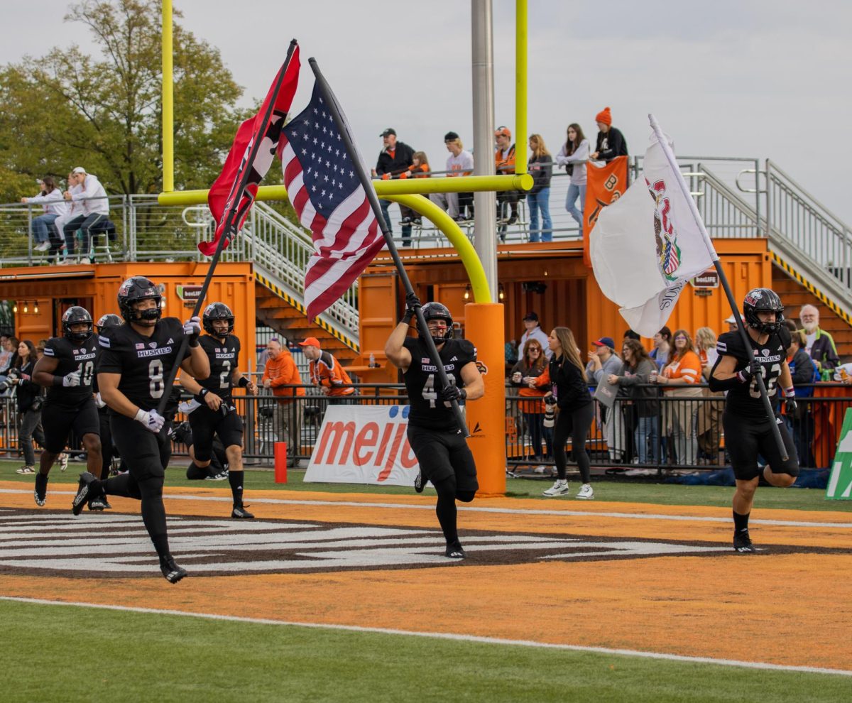 Senior defensive tackle Devonte O’Malley (8) (from left) carries an NIU flag, senior fullback Brock Lampe (49) carries an American flag and redshirt senior tight end Tristen Tewes (82) carries an Illinois flag while running across the end zone to lead the team on the field on Saturday before the game against Bowling Green State University. The Huskies will return Saturday to take on the University of Toledo in the 117th Homecoming game. (Northern Star File Photo)