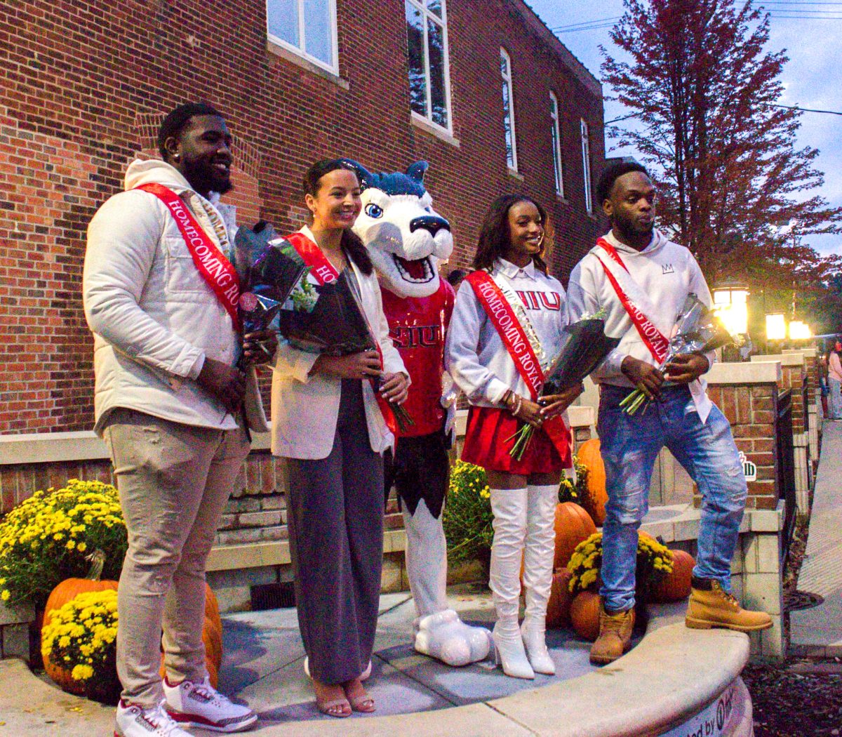 Matthew McConnell (from left), a second-year graduate student in higher education and student affairs, Jasmin Kenzie, an NIU alum, Sydney Thompson, an NIU alum and Nesean Smith, a senior business management major, stand near the Victor E. Huskie statue at the 2023 Homecoming Block Party after they were announced as Homecoming royalty. NIU's 2024 Homecoming events will take place from Oct. 13 through Oct. 20. (Ryanne Sandifer | Northern Star)