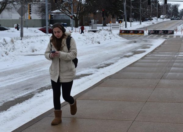 Naomi Langley, a sophomore psychology major, looks at her phone while walking down Normal Road. This winter, fashion trends should be practical and fun. (Northern Star File Photo) 