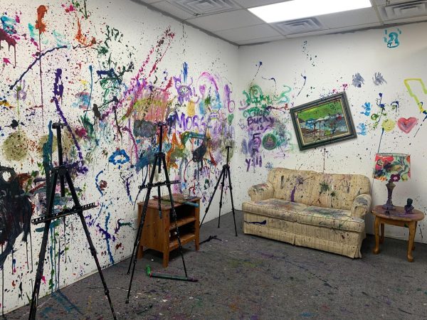 Empty easels and a couch sit in a paint splattered room. Wreckroom DeKalb, 901 Lucinda Ave, Unit G, features a splatter room where customers can pay to splatter paint and de-stress. (Yari Tapia | Northern Star)