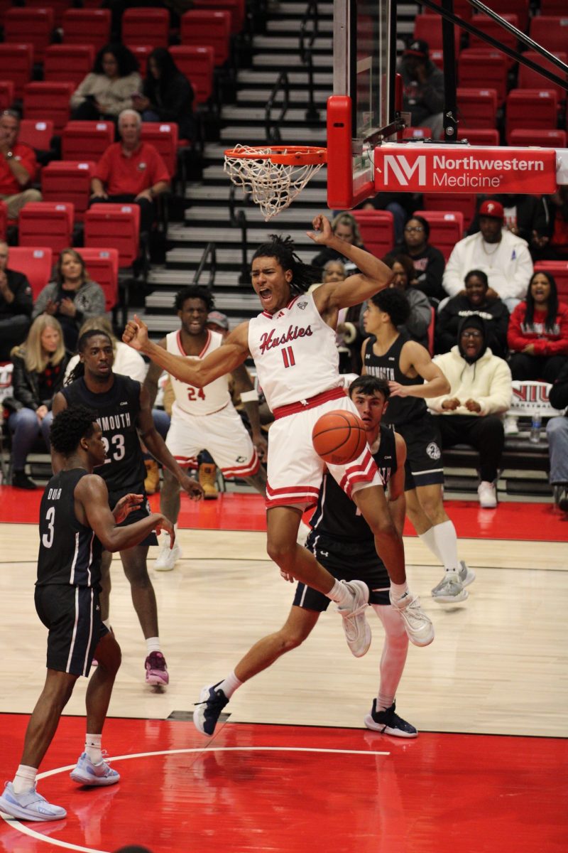 Freshman forward Jayden Mott drops from the rim after a dunk midway through the second half on Tuesday at the Convocation Center. NIU men's basketball scored 24 points in the paint as the Huskies defeated Monmouth University 79-66 on Tuesday. (Tim Dodge | Northern Star)