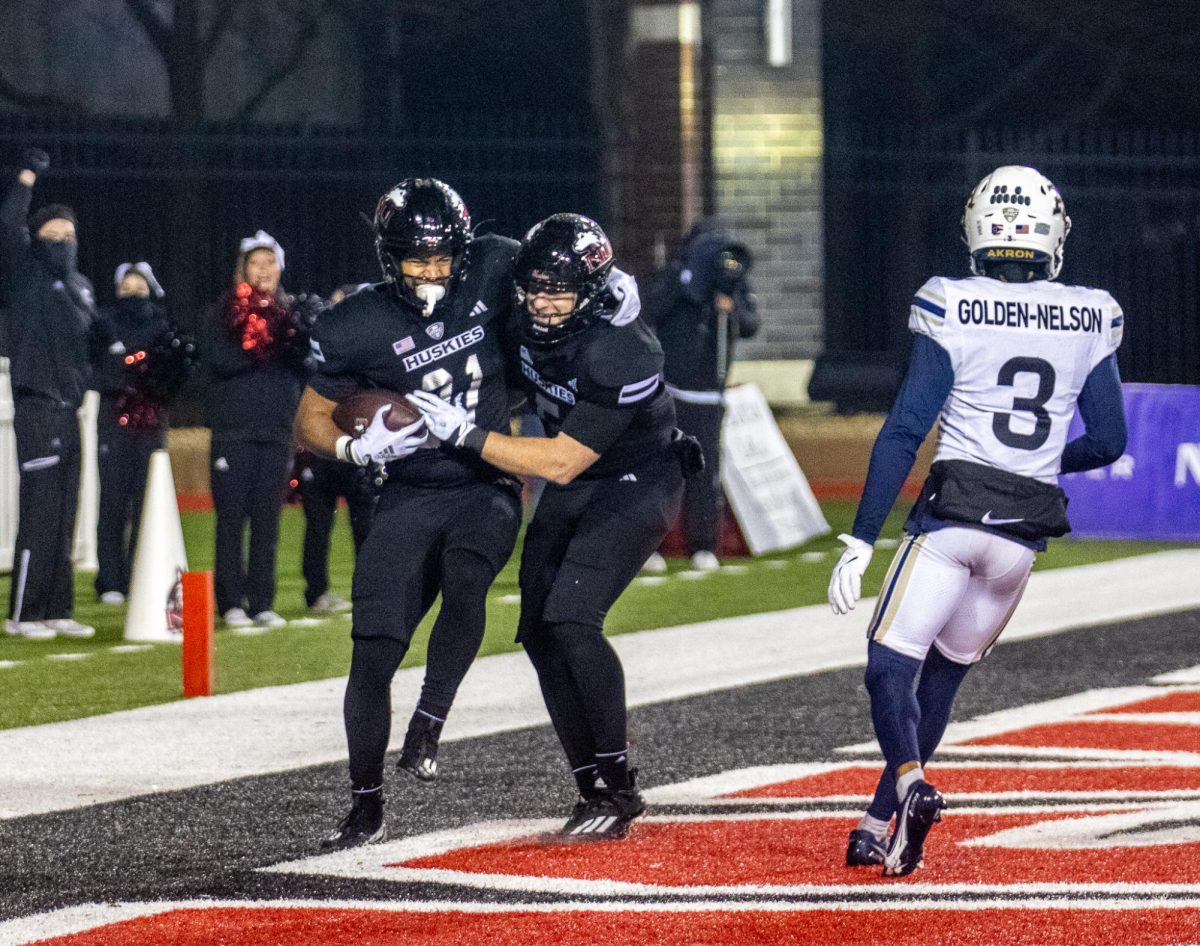 NIU football redshirt junior Justin Lynch (5) celebrates in the endzone with redshirt senior running back Gavin Williams (21) after Williams rushed for a 71-yard touchdown in the fourth quarter Wednesday against the University of Akron Zips. The Huskies defeated the Zips 29-16, advancing to six wins on the season and clinching a bowl game. (Tim Dodge | Northern Star)