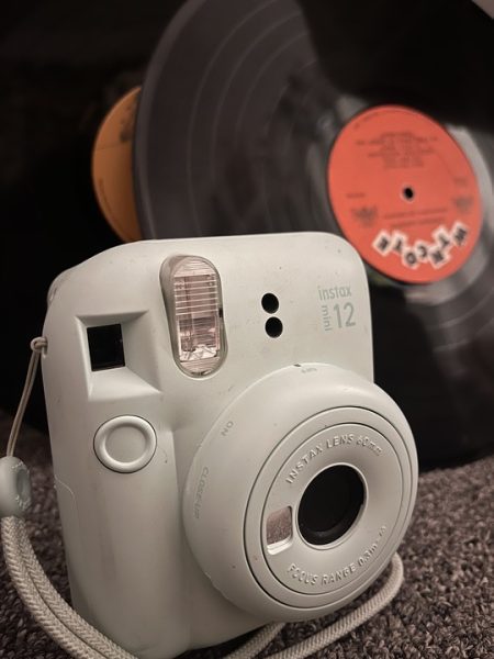 A modern instant camera, “instax mini 12,” sits in front of two vinyl records. Opinion Columnist Sofia Didenko see Generation Z’s appreciation for nostalgic analog technology as a worthy way to jump back in time. (Lucy Atkinson | Northern Star)