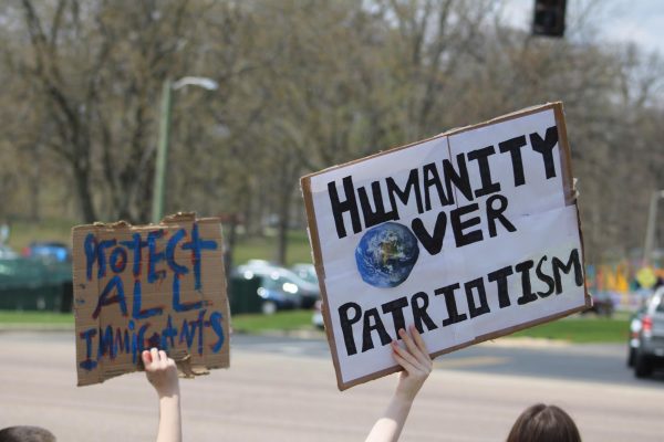 Signs with the words "Protect all Immigrants" and "Humanity over Patriotism" are held in the air during the No Kings protest Saturday. The Northern Star Editorial Board's policy on how we cover international and undocumented students will not change. (Ethan Rodriguez | Northern Star)