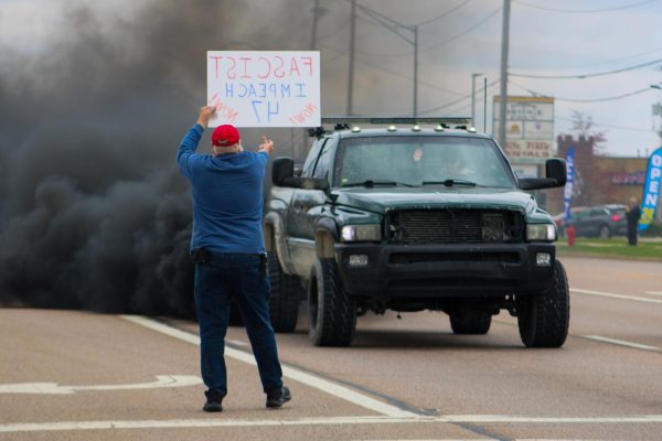 A protester stands on Illinois Route 23 while holding a sign that says “FASCIST IMPEACH 47 NOW” and flips off a truck as it billows smoke from its exhaust pipe. The No Kings protest began just before noon and lasted until around 1:45 p.m. (Ethan Rodriguez | Northern Star)