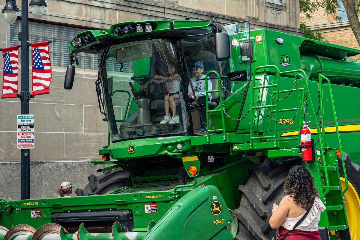 Marcos and Natalia Becerra, children of DeKalb residents Martha and Cosme, pretend to drive a John Deere combine harvester on North Third Street during Corn Fest on Sunday. The John Deere combine harvester, the “StalkMaster,” is one of many types of combine harvesters used to harvest corn. (Totus Tuus Keely | Northern Star)