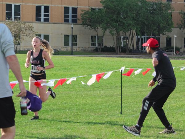 NIU cross country head coach Juan Carrillo encourages then-senior runner Olivia Southby as she runs the course at the NIU Huskie Opener on Sept. 6, 2024. NIU cross country kicks off its season on Friday at the Fighting Illini Open.  (Totus Tuus Keely | Northern Star)