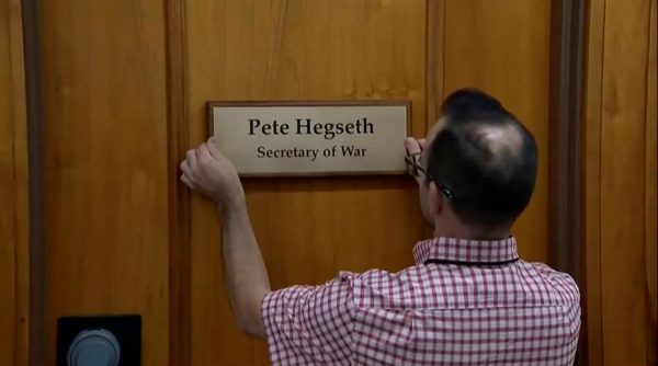 A worker places a plaque that reads "Pete Hegseth - Secretary of War" after President Donald Trump signed an executive order to rename the Department of Defense the "Department of War." Opinion Columnist Ethan Ernst argues that Donald Trump changing the name of the Department of Defense to the Department of War is a waste of time. (Reuters TV | Pool)