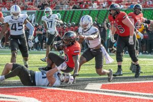 NIU redshirt senior running back Chavon Wright (10) falls into the end zone for a 2-yard touchdown as he's brought down by The College of the Holy Cross junior linebacker Cam Santee (21) during the fourth quarter of NIU's season opener on Saturday at Huskie Stadium in DeKalb. The score was the Huskies' first offensive touchdown of the 2025 season. (Totus Tuus Keely | Northern Star)