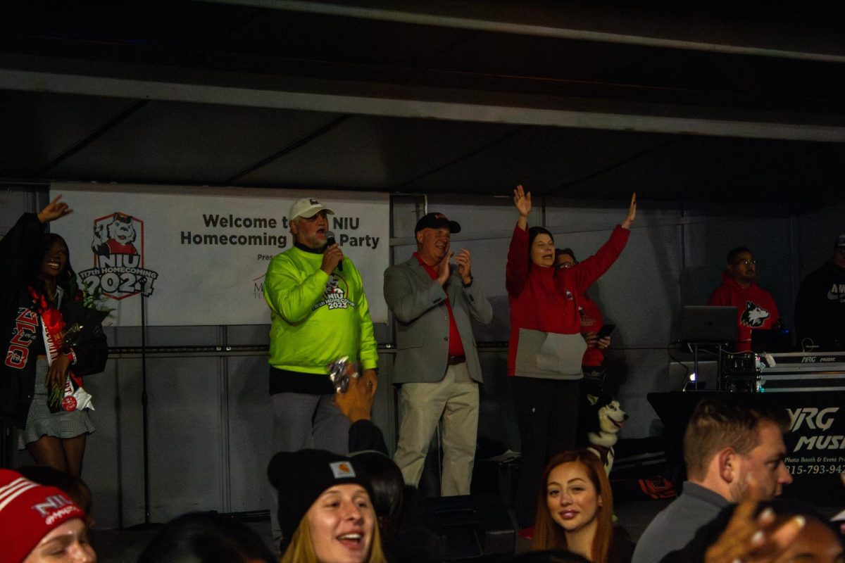 A long-time NIU fan leads the Huskie fight song on the stage next to DeKalb Mayor Cohen Barnes (middle) and NIU President Lisa Freeman (right) at the 2024 Homecoming Block Party. NIU is kicking off its 118th Homecoming, the oldest in Illinois, providing a week of fun for staff, students and the community. (Northern Star file photo)
