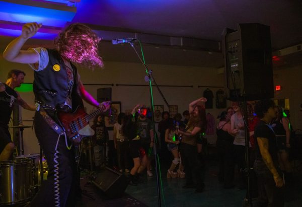 JM Graveside, bassist of Kozmic Kicks, raises his arm mid-riff as a crowd dances at Fargo during the 7–10 p.m. show, which featured four local bands. The bands played covers from Nirvana, Chevelle, and Deftones alongside original tracks. (Brynn Krug | Northern Star)