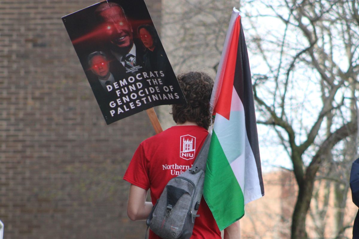 An NIU student stands during a Palestine protest holding a Palestinian flag and a sign that says "Democrats fund the genocide of Palestinians.” Opinion Columnist Alyssa Aarvig argues that supporting Palestine isn't inherently anti-Semitic. (Ethan Rodriguez | Northern Star)