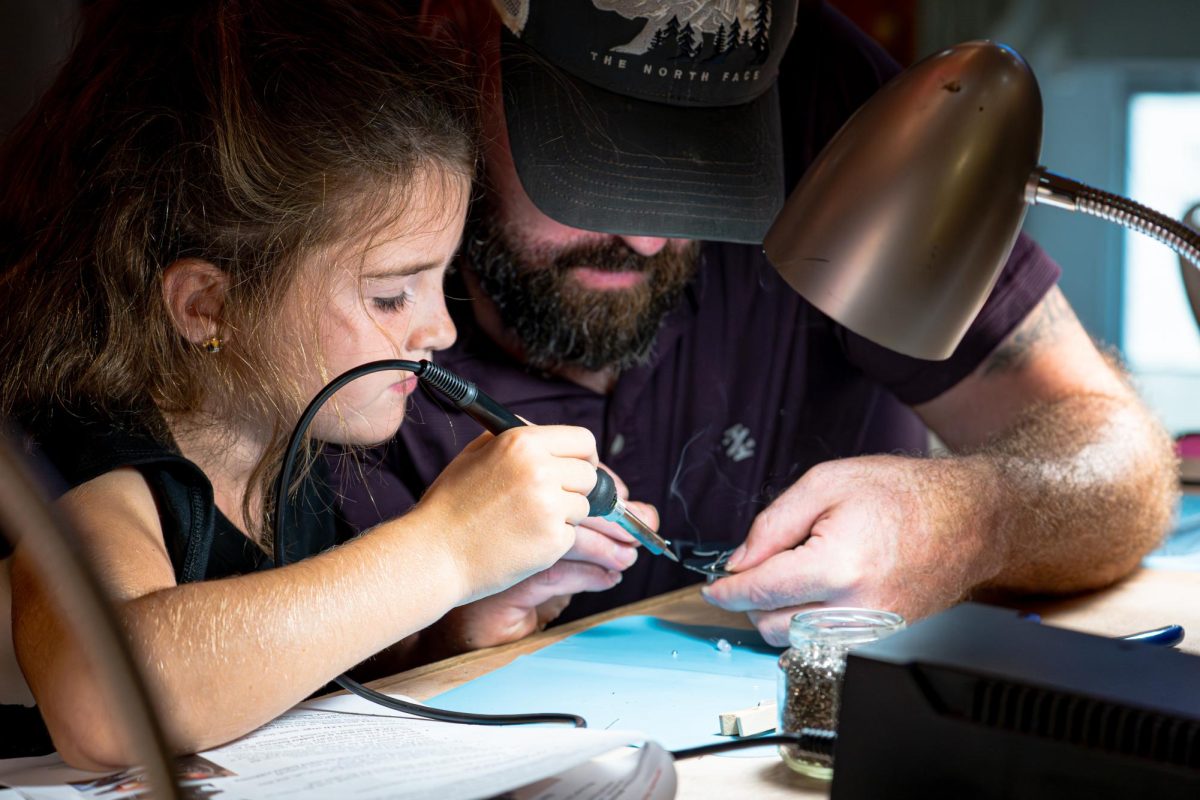 Mila (left) and her father Mike Meegan, both Ottawa residents, solder a connection for a “blinkie” at the Build-a-Blinkie station on Saturday at STEM Fest inside of the Duke Ellington Ballroom in the Holmes Student Center. A “blinkie” is a small board cut into a design with flashing LEDs, supplied by the 501(c)3 organization Build-a-Blinkie. (Totus Tuus Keely | Northern Star)