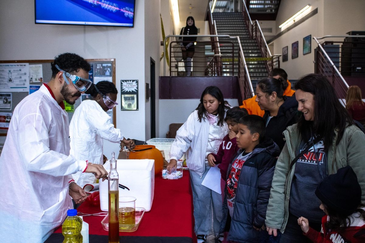 Junior pre-professional chemistry major Esteban Saenz (from left) and sophomore biology major Christine Davis perform a variety of experiments for families on Saturday during Revenge of the Haunted Labs in the lower lobby area of La Tourrette Hall. The event had over 100 student volunteers to help run experiments. (Ethan Rodriguez | Northern Star)