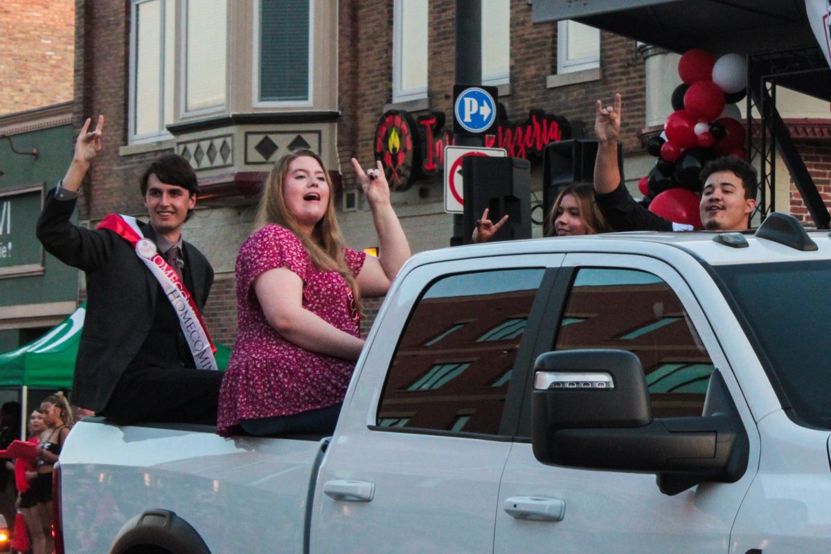 J.C. La Barbera, a senior mechatronics engineering major (from left); Erin Uhrine, a senior early education with special ed with ELS major; Jocelyn Campos Diaz, a senior physical education major; and Ghaika Vera, a senior finance major, make Huskie hand signs as they ride in the bed of a white pickup truck on Thursday during the parade section of the NIU Homecoming Block Party in downtown DeKalb. La Barbera, Uhrine, Diaz and Inara Perryman, a junior political science major, were all declared the winners of the NIU 118th Homecoming Court. (Ethan Rodriguez | Northern Star)