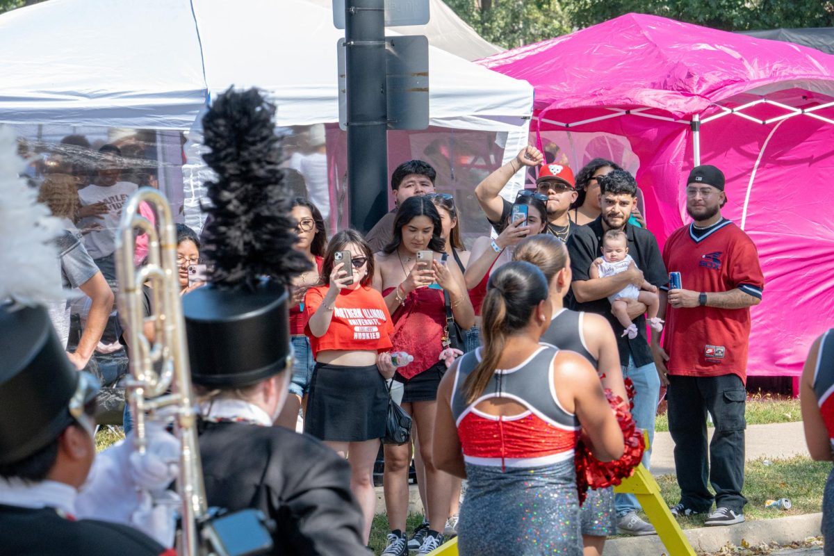 People record the NIU Marching Band members and cheerleaders as they march past on Stadium Drive South after their completion of their Yard performance on Saturday. NIU football will return home at an announced time on Oct. 25 against Ball State University. (Totus Tuus Keely | Northern Star)