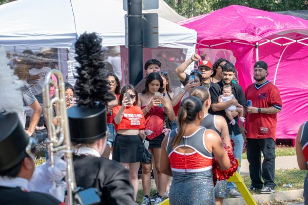 People record the NIU Marching Band members and cheerleaders as they march past on Stadium Drive South after their completion of their Yard performance on Saturday. NIU football will return home at an announced time on Oct. 25 against Ball State University. (Totus Tuus Keely | Northern Star)
