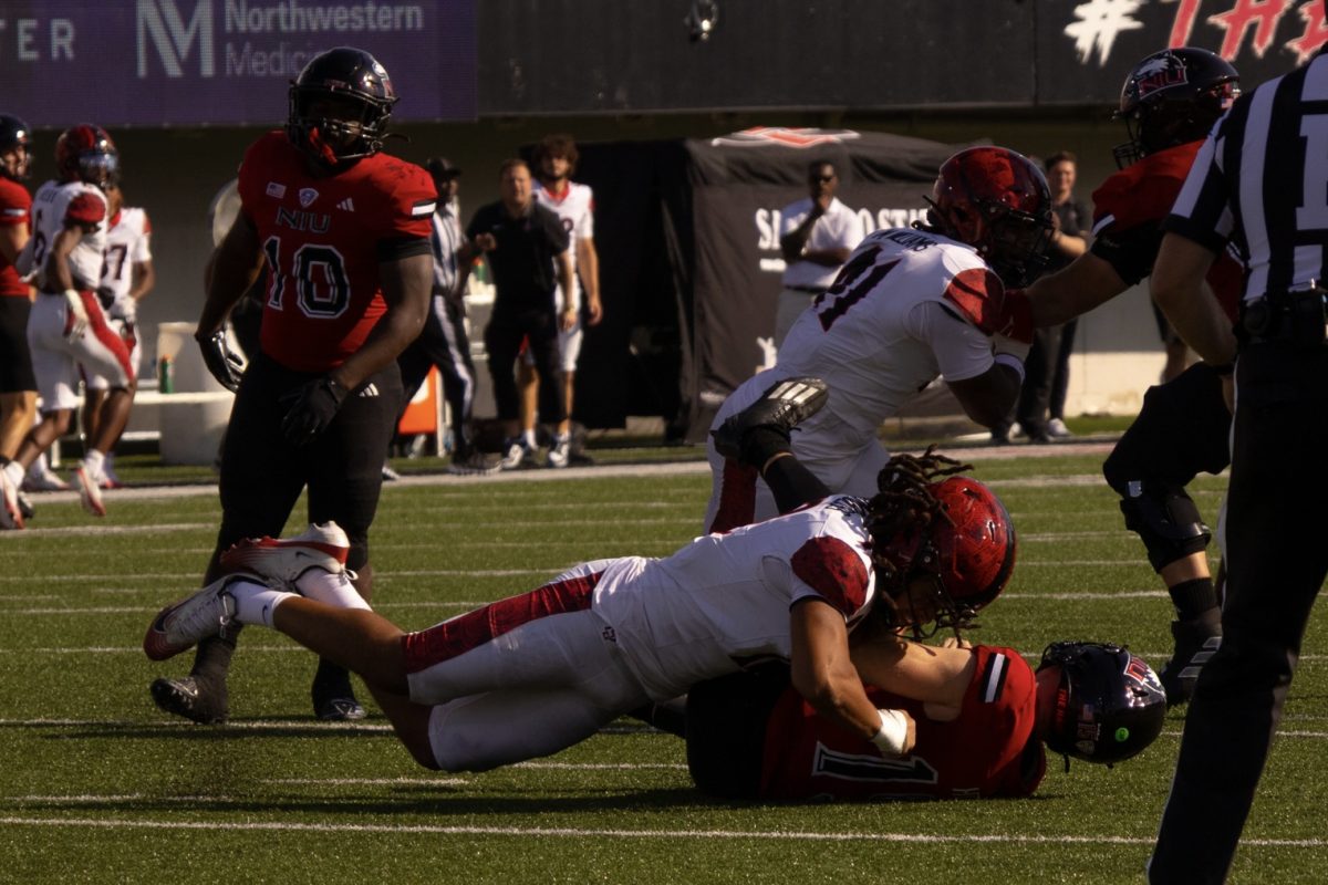 NIU redshirt senior running back Chavon Wright (10) looks on as redshirt sophomore quarterback Josh Holst, bottom, is sacked by San Diego State University sophomore linebacker Owen Chambliss during a football game on Sept. 27 at Huskie Stadium in DeKalb. NIU's 6-3 loss to San Diego State was the third among the Huskies' ongoing six-game losing streak. (Alexia Beck | Northern Star)