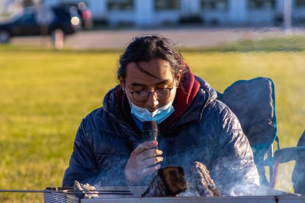 Fernando Marroquin, a graduate world music student, reads a "Pie De Lana" near a bonfire. The Leyendas and Myths Bonfire happened from 4 p.m to 5:30 p.m on Monday by the Outdoor Recreation Sports Center. (Northern Star | Ethan Rodriguez)