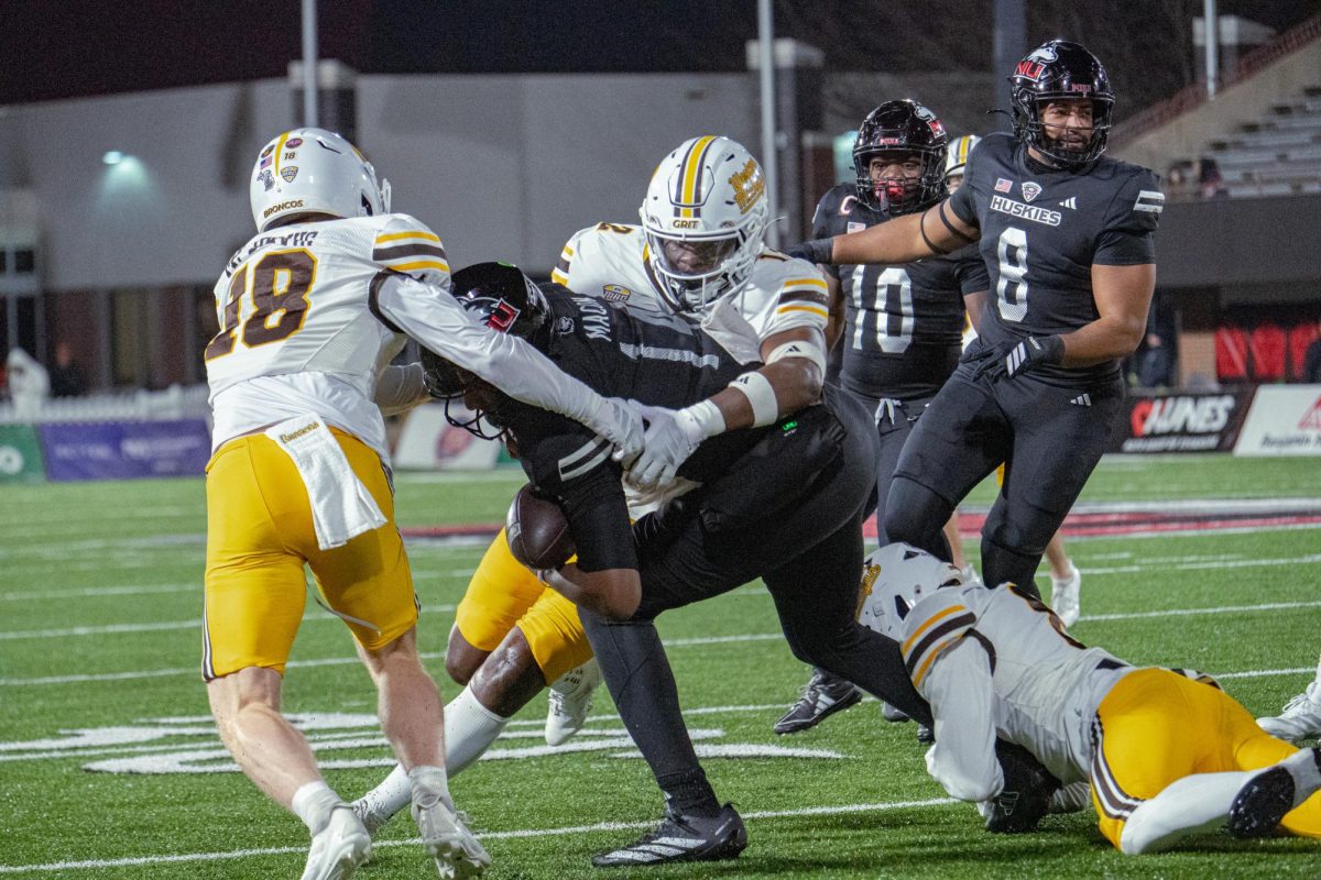 NIU redshirt junior quarterback Jalen Macon (14) is tackled for a 1-yard loss by Western Michigan University redshirt junior linebacker Dillon Moore (12) during the first quarter of a football game on Tuesday night at Huskie Stadium in DeKalb. Macon was 1-of-7 passing for 5 yards before he was benched in the late stages of NIU’s 35-19 loss. (Totus Tuus Keely | Northern Star)