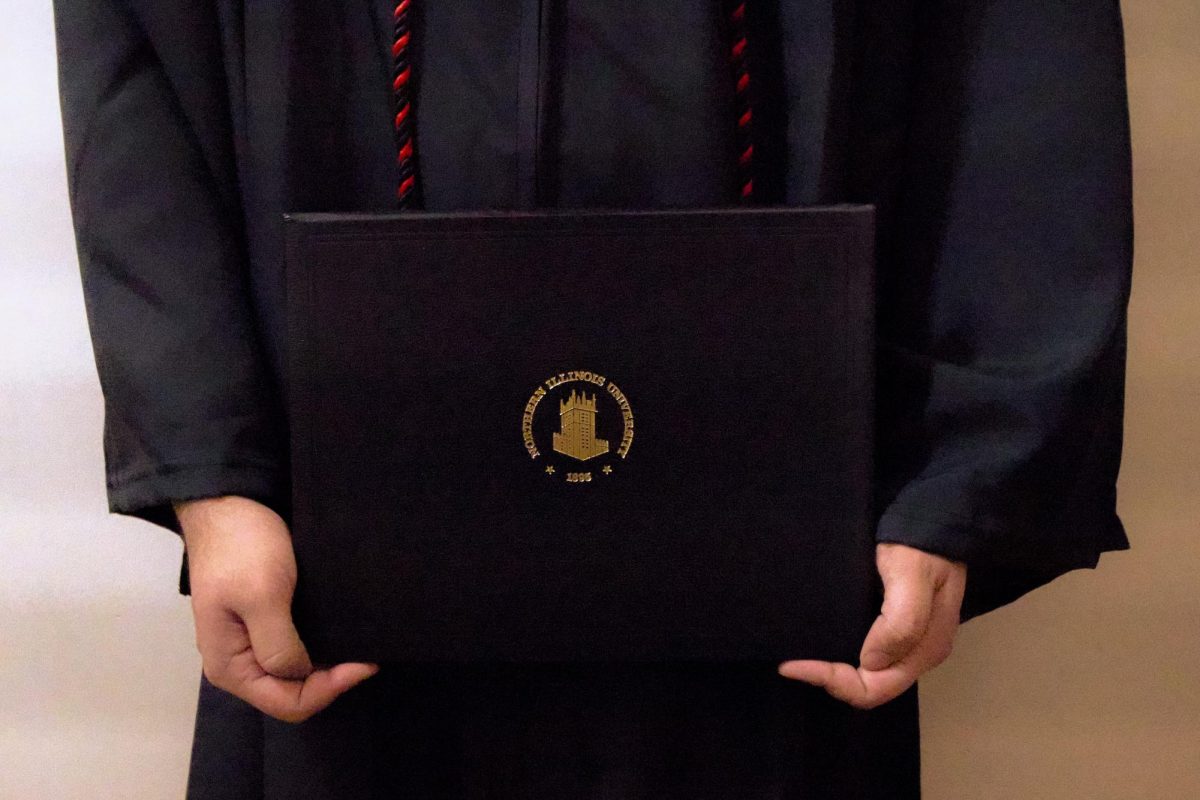 NIU graduation attire and diploma are posed for a picture. Opinion Columnist Ethan Ernst believes degrees are less valuable due to the evolving professional world, but not entirely obsolete either. (Isabella Froh | Northern Star)