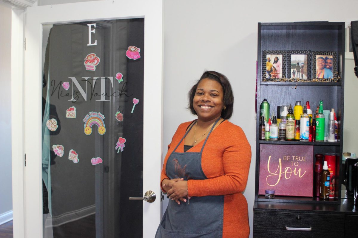 Owner Nia Hill stands inside her salon, Nia’s Touch, 224 E. Lincoln Highway, Suite E, beside a shelf of hair-care products and framed family photos. Nia’s Touch is a hair braiding and care salon open from 9 a.m. to 6 p.m. Mondays, Wednesdays, Fridays and Saturdays and 9 a.m. to 3 p.m. on Tuesdays and Thursdays. (Kaler Munoz Ramirez | Northern Star)