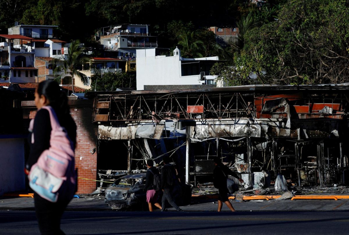 People walk past a store and a car on Thursday in Puerto Vallarta, Mexico, that were set on fire by members of organized crime in the aftermath of "El Mencho’s” death. Assistant Opinion Editor Lupita Diaz believes the killing of El Mencho was an ill-advised decision that will only lead to further violence and public scrutiny for Mexico. (REUTERS | Daniel Becerril)