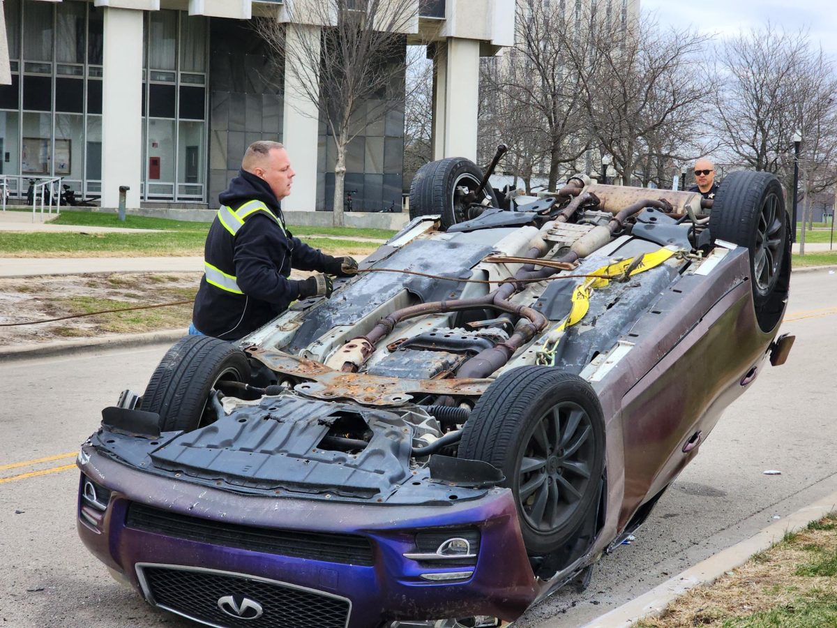 Adam Benn, manager at Accurate Towing and Recovering, places the hook for the winch after the rollover at 2:48 p.m. Wednesday on Lucinda Avenue, south of Stevenson Towers. Bystanders at the NIU baseball game nearby described the crash as thunder, gaining the attention of Stevenson residents looking out their window. (Totus Tuus Keely | Northern Star)