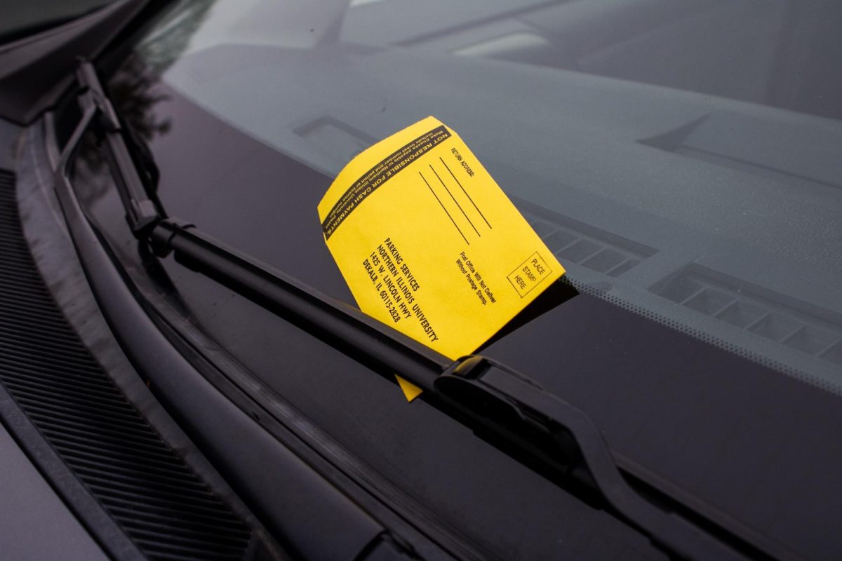 A parking ticket from NIU Parking Services sits under the windshield of a car in the Peter Campus Life Building student lot. The student lot near the Campus Life Building is among the heavily ticketed areas contributing to the 7,546 citations issued in fall 2025. (Ethan Rodriguez | Northern Star)